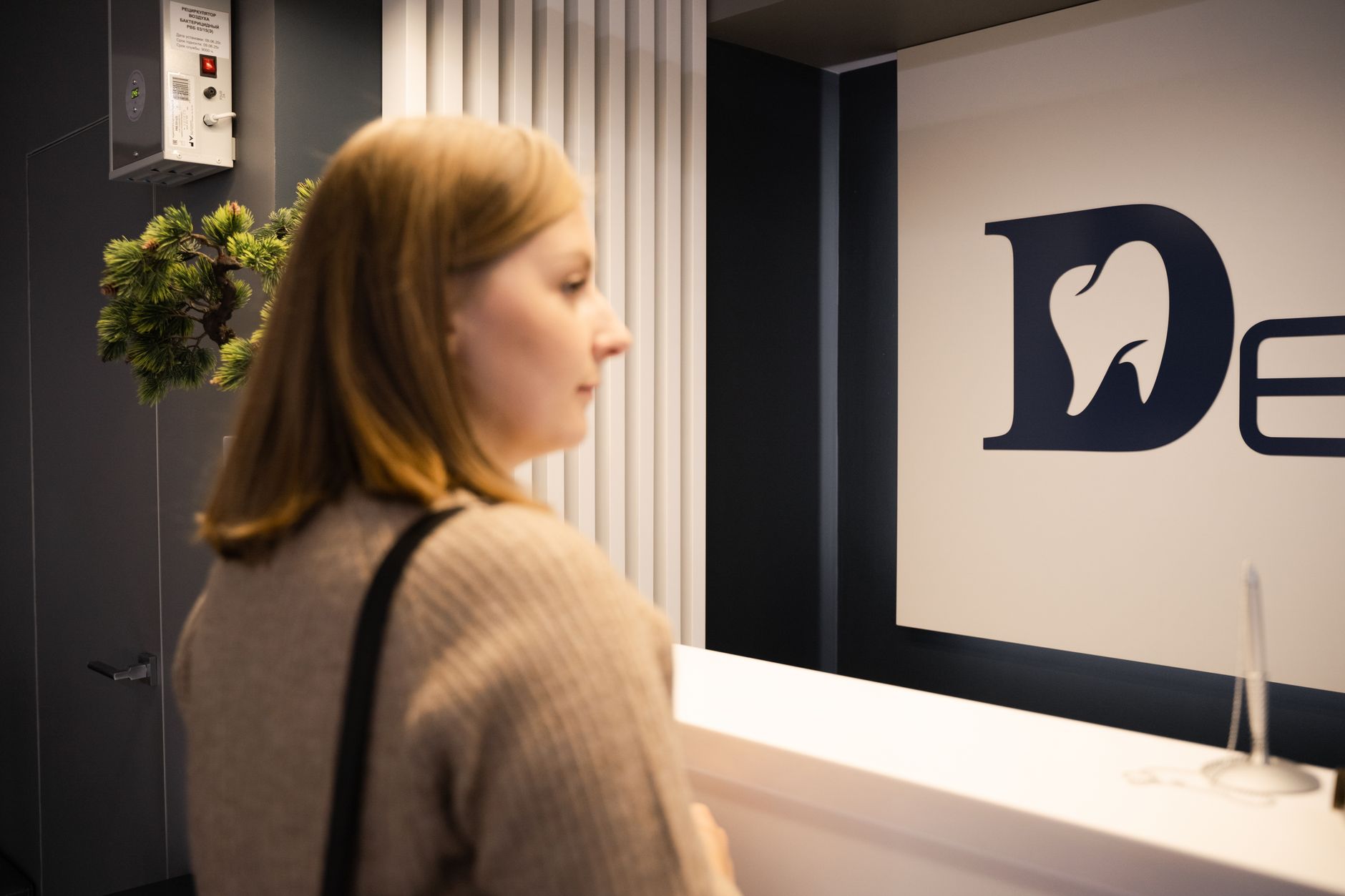 Young woman stands at a dental office reception, side view, casual attire.