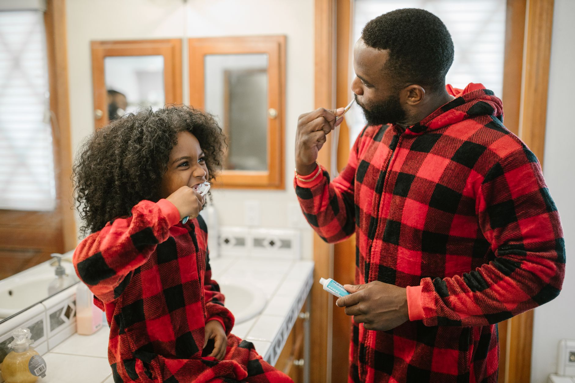 Father and daughter in pajamas practicing morning hygiene in the bathroom.